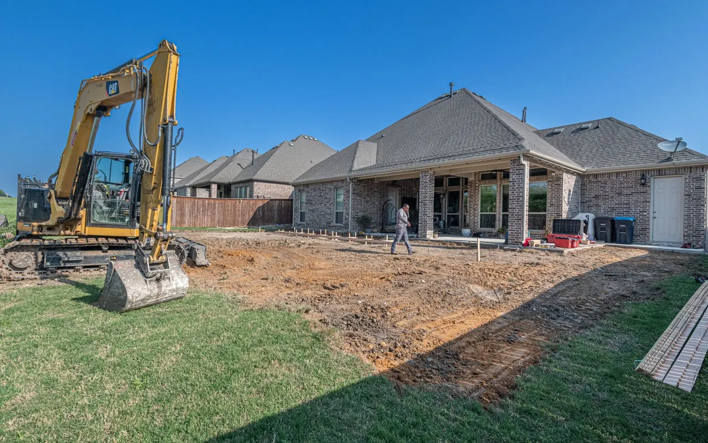 Machinery excavating and grading ground during backyard patio construction