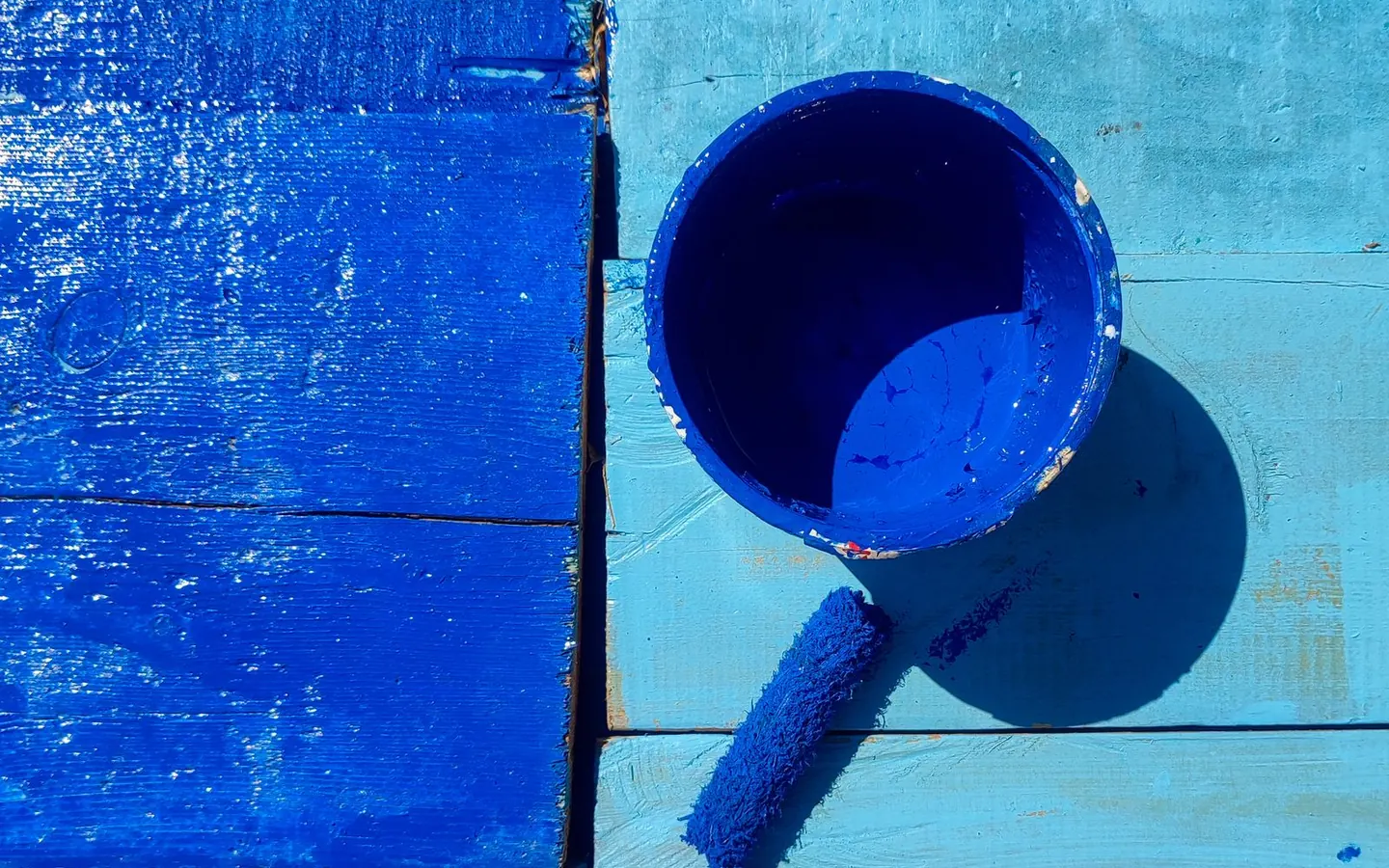 Blue paint, a roller and a painted wooden surface