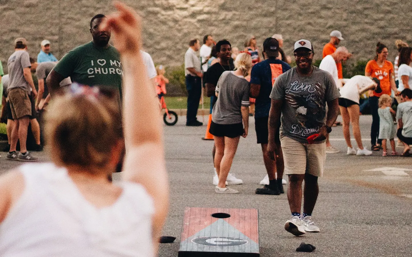Players and onlookers around cornhole boards at an outdoor community event