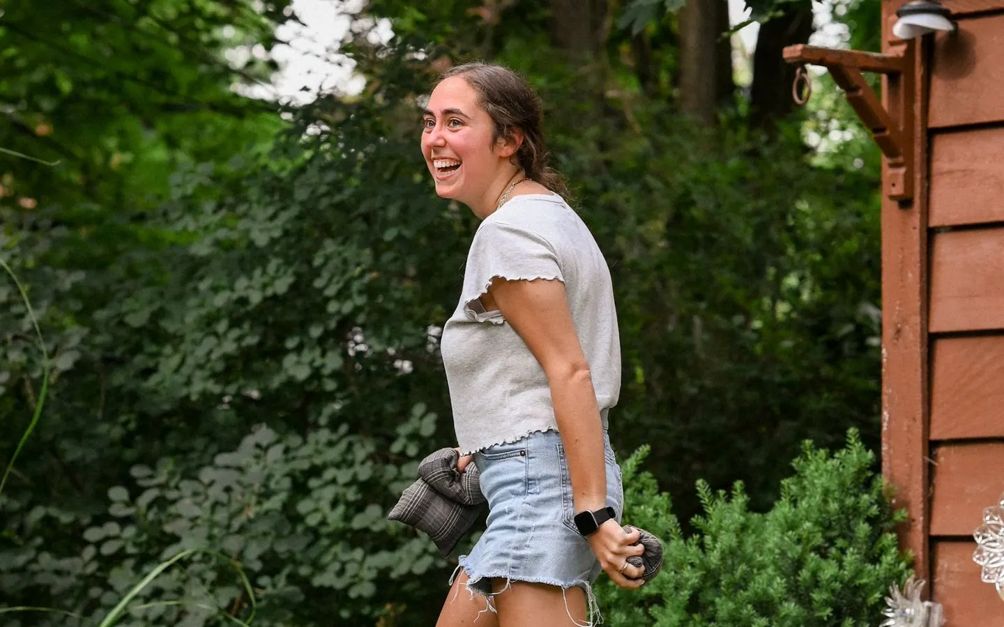 A woman playing cornhole in a leafy backyard
