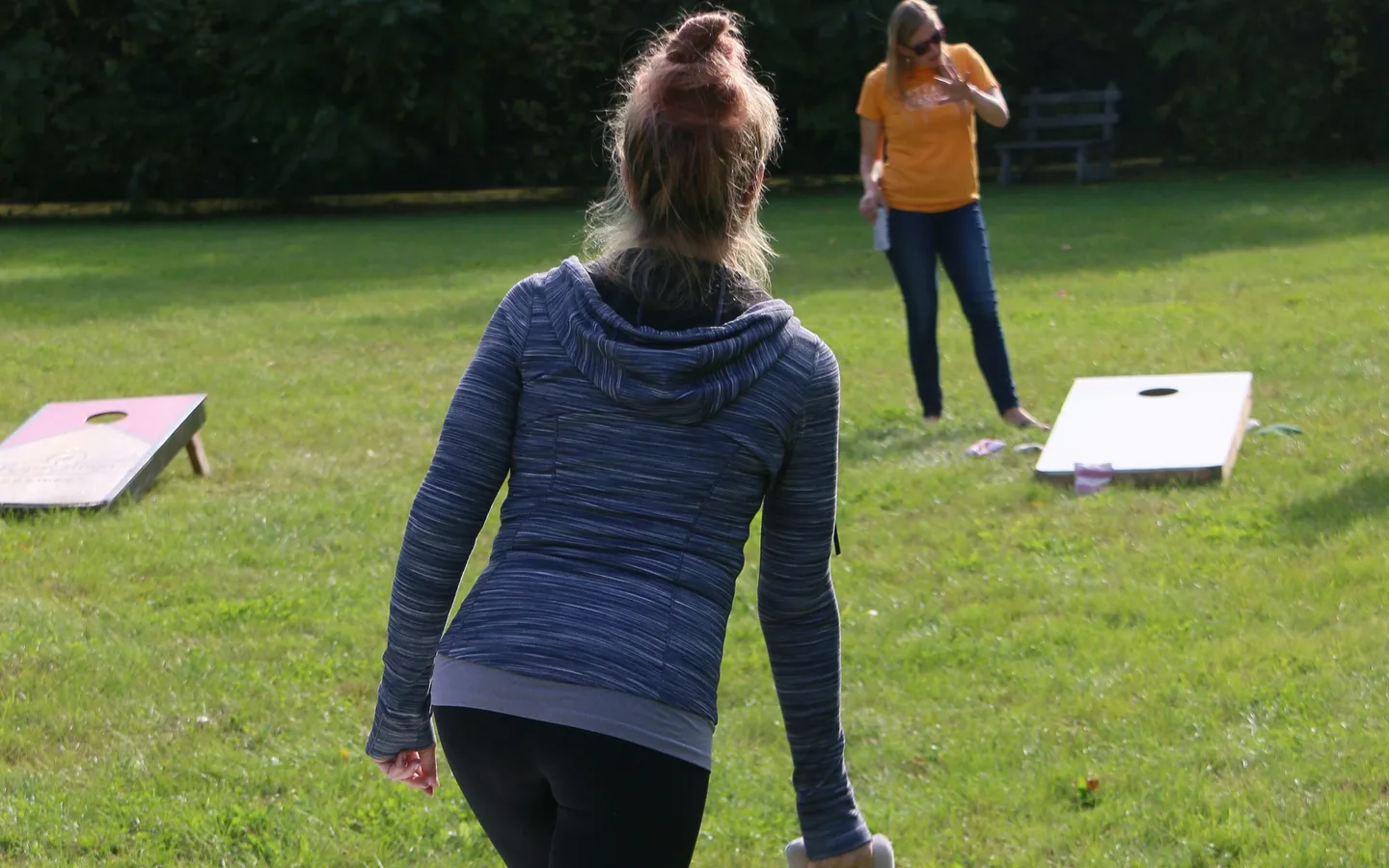 A woman preparing an underhand cornhole toss toward a board on a grassy lawn