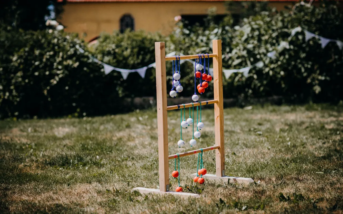 A wooden ladder-style toss game with rungs and rope-and-ball bolas set up on a backyard lawn