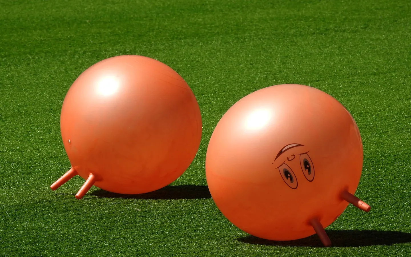 Two orange hopper balls on a green lawn, ready for a game