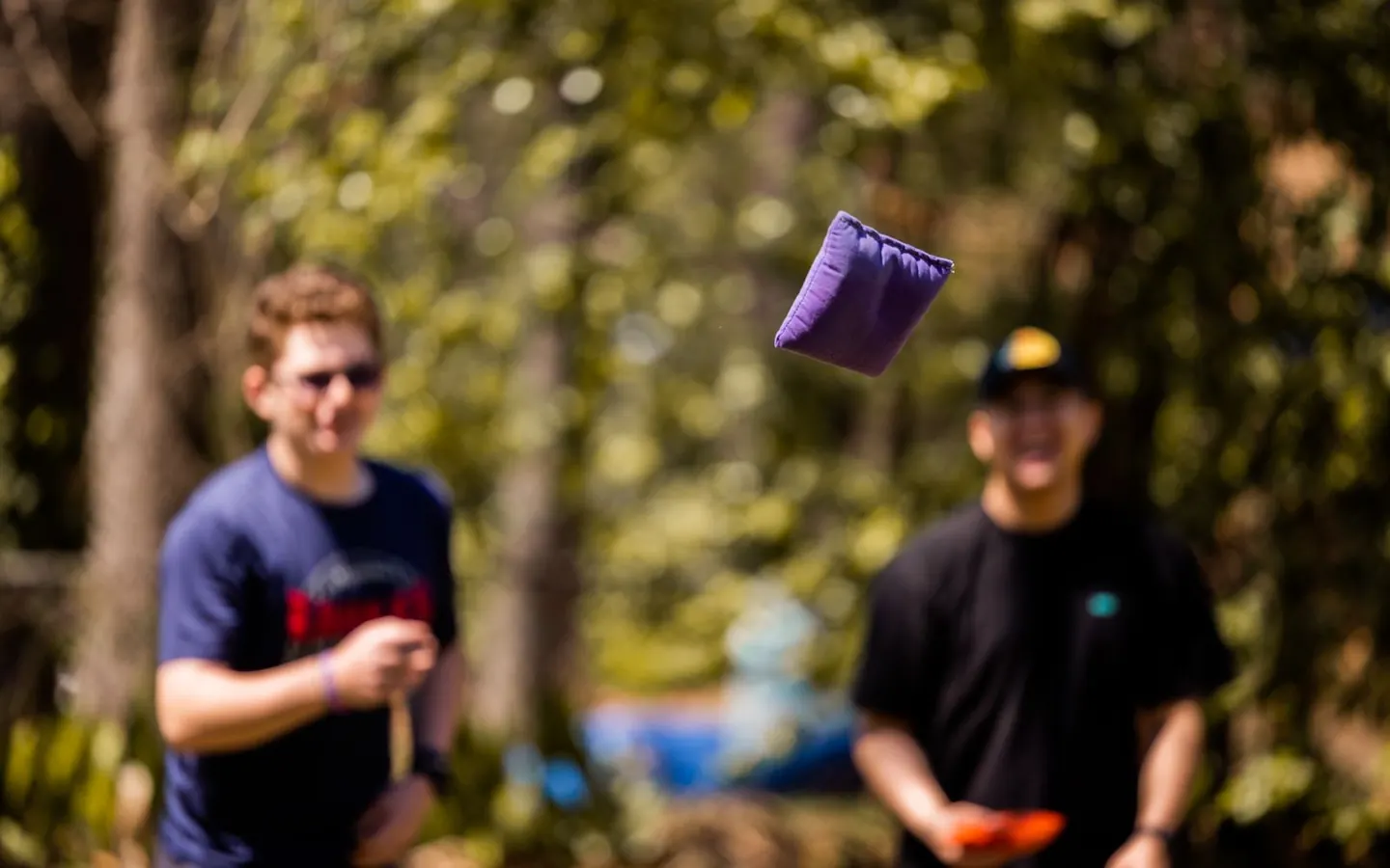 Two adults playing a bean bag toss game outdoors on a sunny day