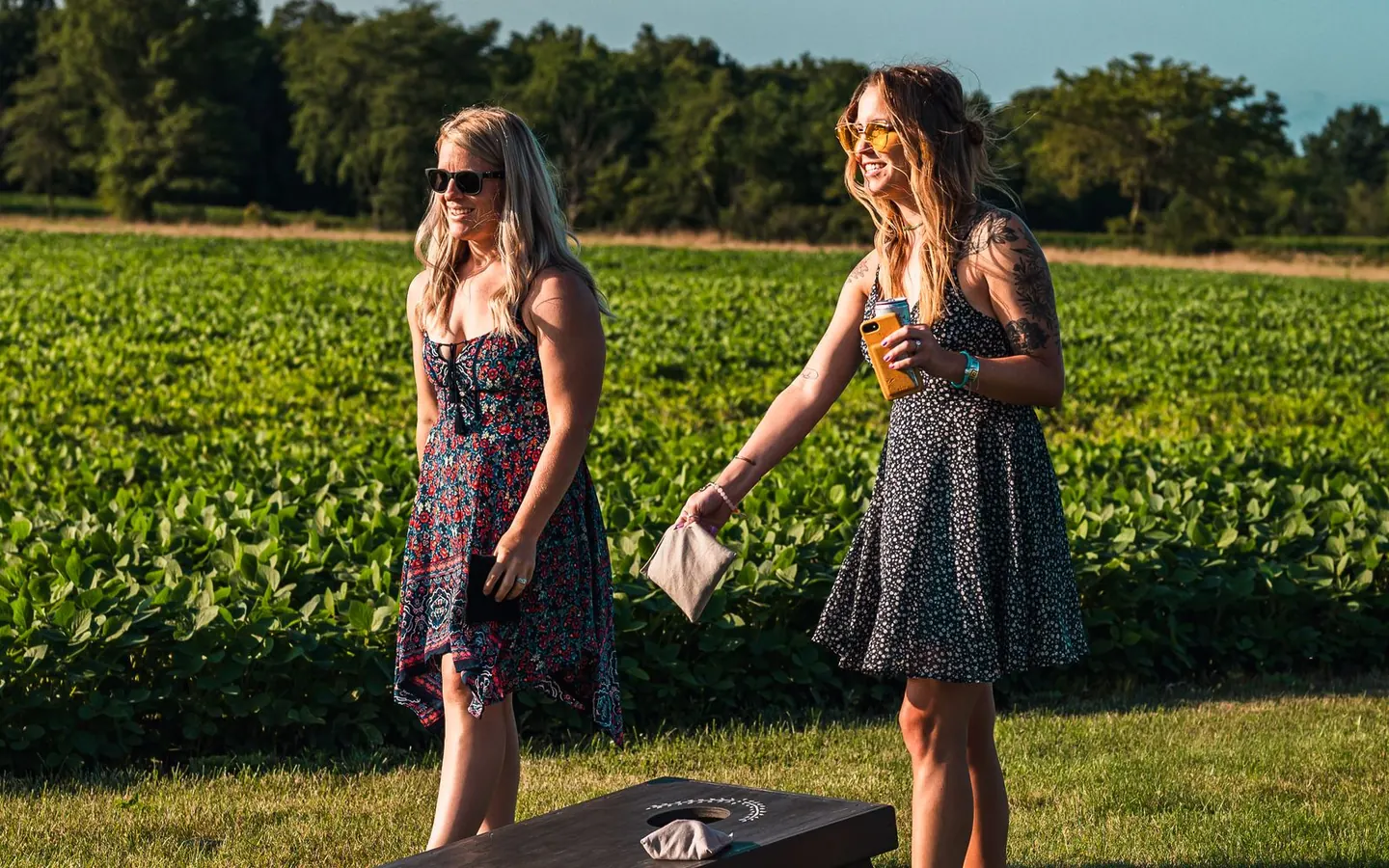 Two women playing cornhole on a sunny grass lawn