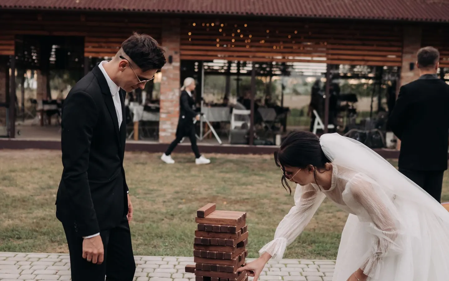 A bride and groom playing a wooden block-stacking game outdoors at their reception